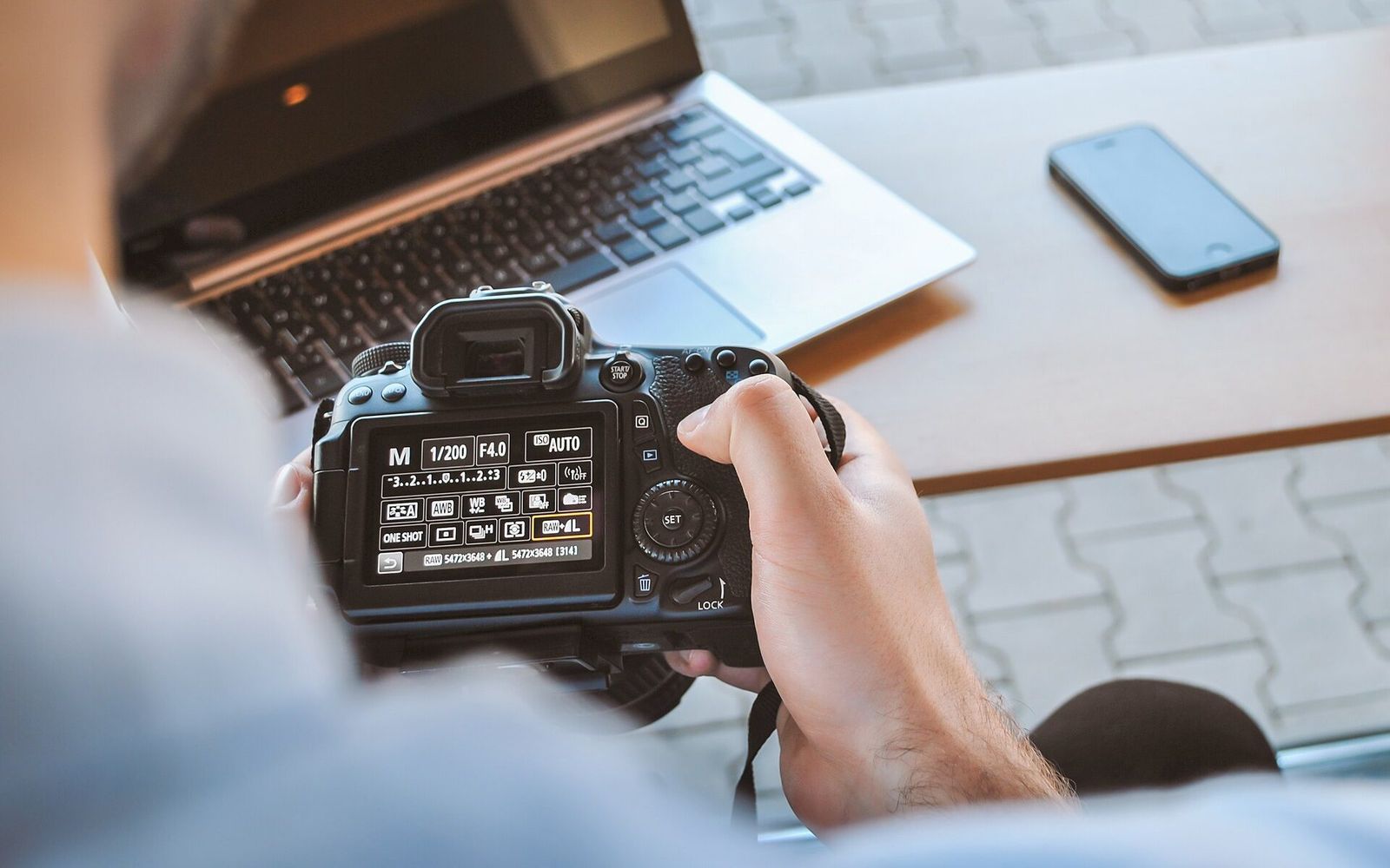 Hands holding a camera in front of a laptop